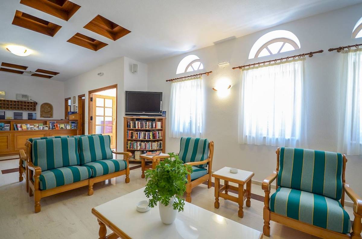 Proteas Hotel & Suites Lobby mit Sofas, Fernseher und Bücherregal.