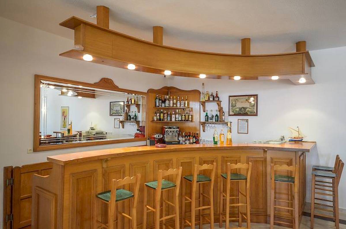 Rezeption und Bar im Proteas Hotel & Suites mit hölzerner Einrichtung und grünen Stühlen.