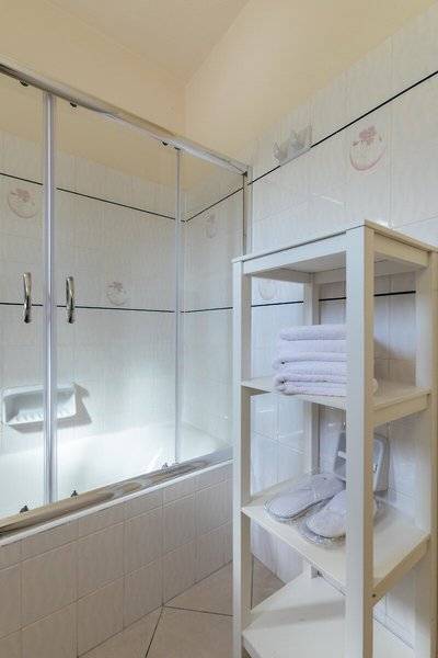 Badezimmer mit einer Dusche und einem Schrank, der Handtücher und Hausschuhe bereithält.