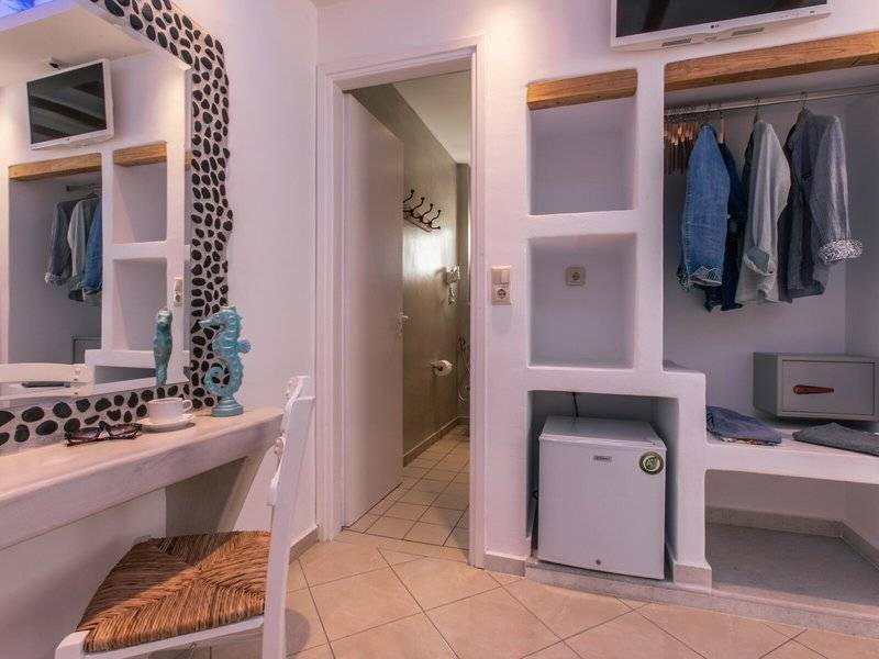Innenansicht eines Zimmers im Mikri Vigla Hotel mit Schreibtisch, Stuhl und Ankleidebereich.