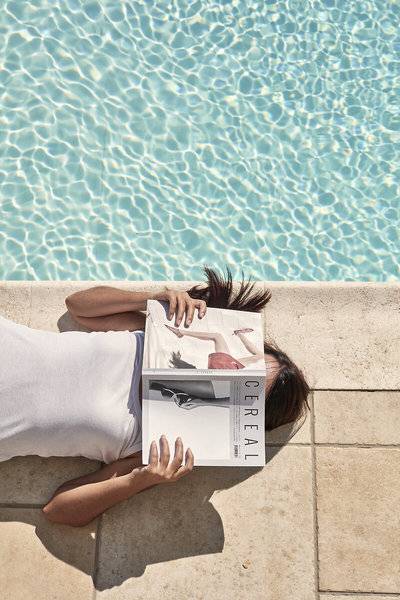Eine Frau liegt am Pool und liest ein Magazin.