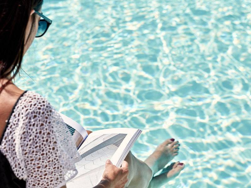 Frau sitzt im Schwimmbad und liest ein Buch