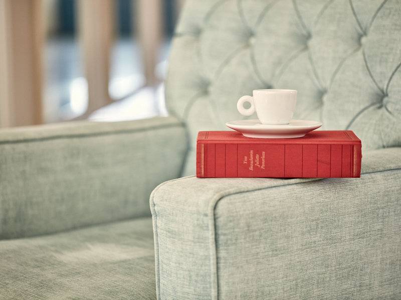 Rotes Buch auf einem grauen Sofa mit einer weißen Tasse und Untertasse