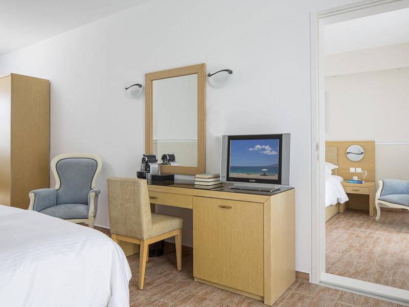 Innenansicht eines Hotelzimmers im Lagos Mare mit Schreibtisch, Fernseher, Stühlen und Spiegel.