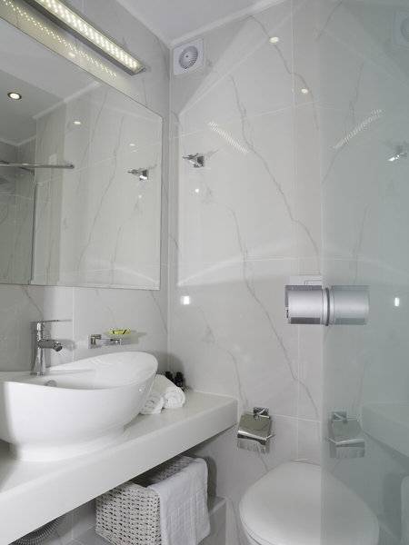 Modernes Badezimmer im Amaryllis Paros Beach Hotel mit weißen Fliesen, einem Waschbecken und einem Spiegel.