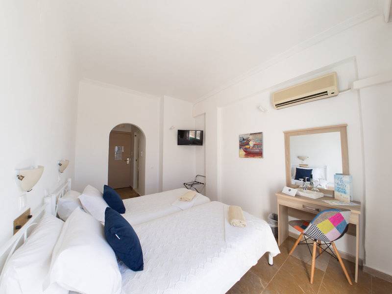 Schlafzimmer im Amaryllis Paros Beach Hotel mit zwei Betten, weißem Bettwäsche, blauen Kissen und einem Fernseher.