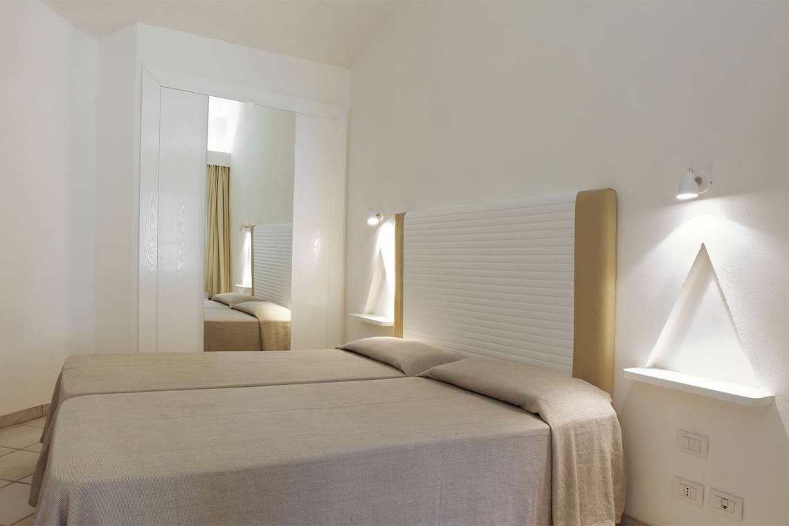 Innenansicht eines Doppelzimmers im Mare Pineta Hotel mit zwei Betten, Spiegel und Nachttischen.