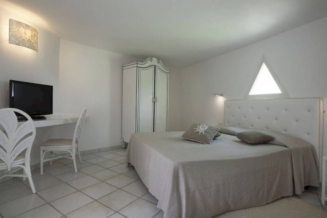 Innenansicht eines Schlafzimmers im Mare Pineta Hotel mit weißem Bett, Schreibtisch und Fernseher.