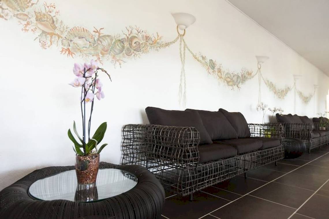 Lobby-Lounge des Mare Pineta Hotels mit schwarzen Sofas und Tisch mit Blumenvase.