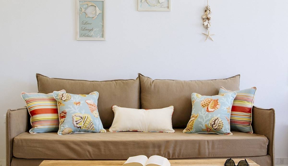 Wohnzimmer mit einem braunen Sofa, verschiedenen gemusterten Kissen und einem offenen Buch auf einem Tisch.