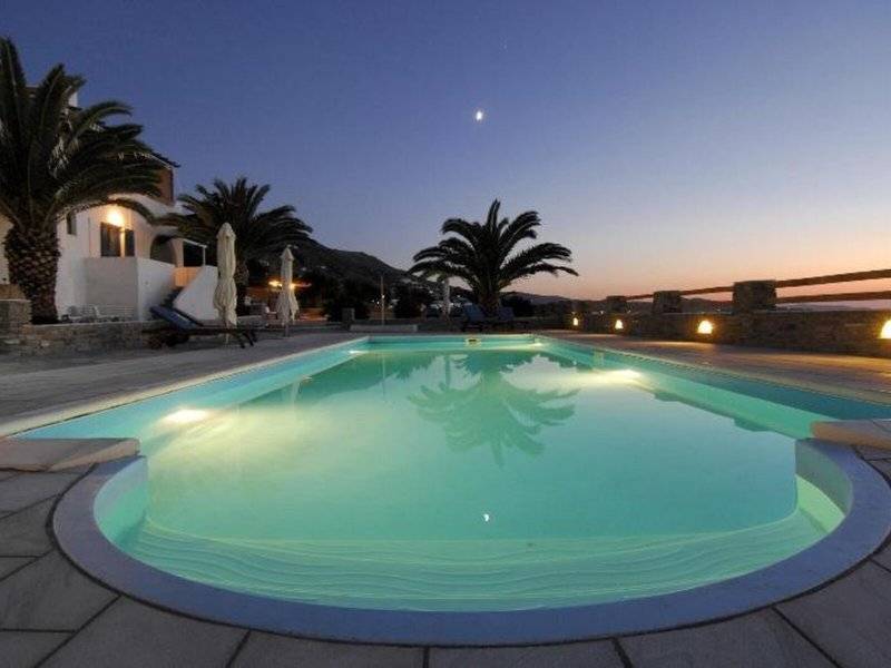Ein Swimmingpool im Garten des Pyrgaki Hotels bei Nacht, beleuchtet und umgeben von Palmen und Sonnenliegen.