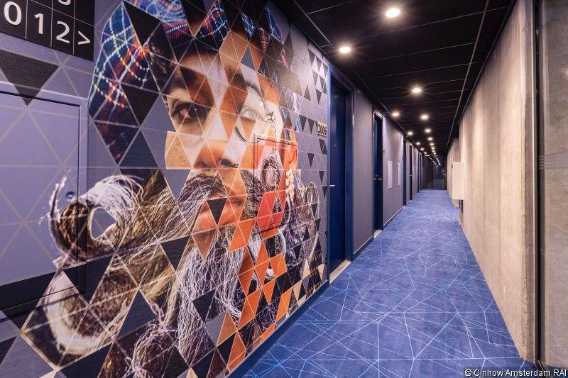 Korridor des nhow Amsterdam RAI Hotels mit einer großen Wandkunst, die ein geometrisches Porträt zeigt.