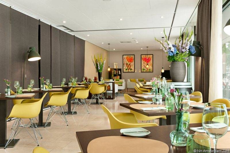 Innenbereich des NH Amsterdam Zuid Hotels mit gelben Stühlen und gedeckten Tischen