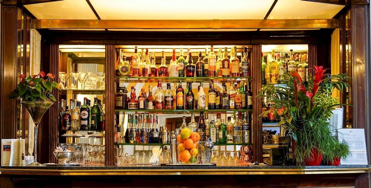 Die Bar im Bettoja Hotel Massimo d'Azeglio mit vollbestückten Regalen, Gläsern, Früchten und Pflanzen.