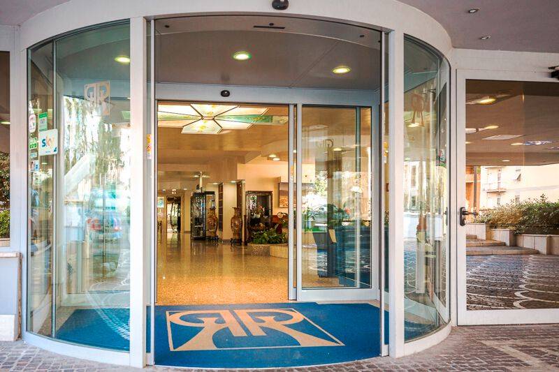 Der Eingang des Pineta Palace Hotels mit gläsernen Drehtüren und blauem Teppich mit Logo.