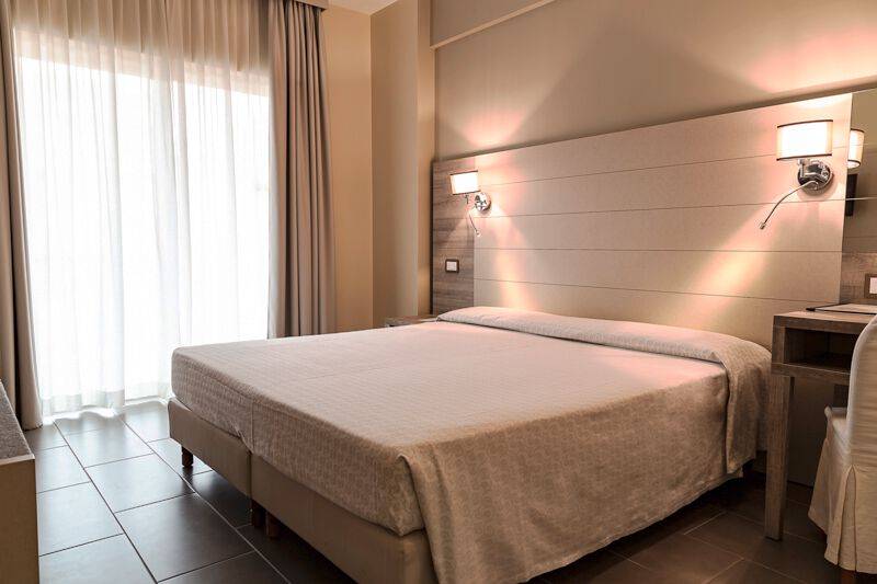 Hotelzimmer im Pineta Palace mit einem Bett, Schreibtisch und Wandlampen.