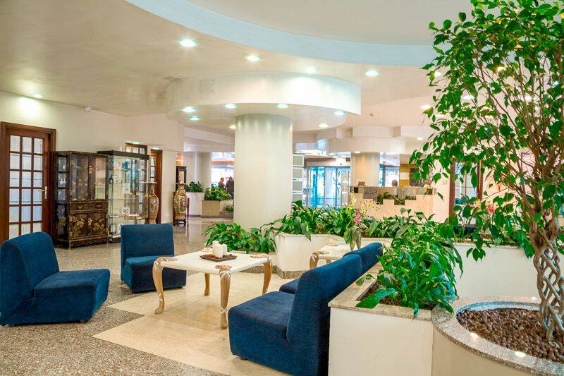Foyer des Pineta Palace Hotels mit blauen Sesseln, einem weißen Tisch und grünen Pflanzen.