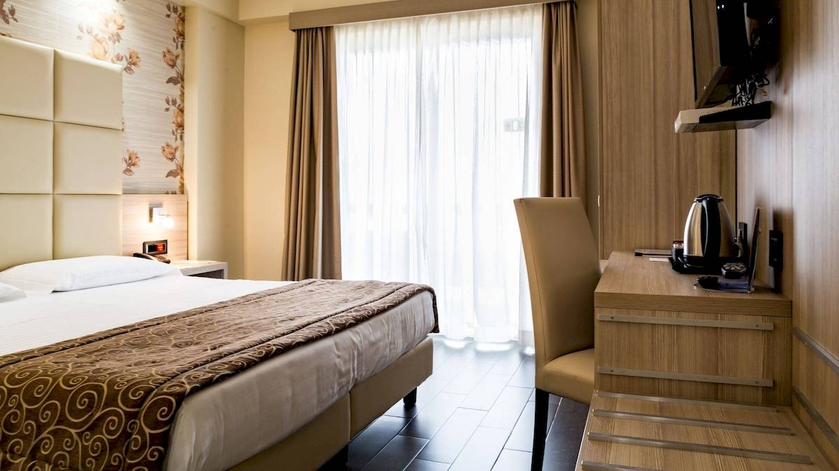 Hotelzimmer im Pineta Palace mit Bett, Schreibtisch und Fenstern.