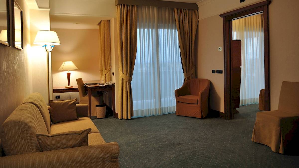 Innenansicht eines Hotelzimmers im Pineta Palace mit Sofa, Schreibtisch, Stühlen und Fenstern.