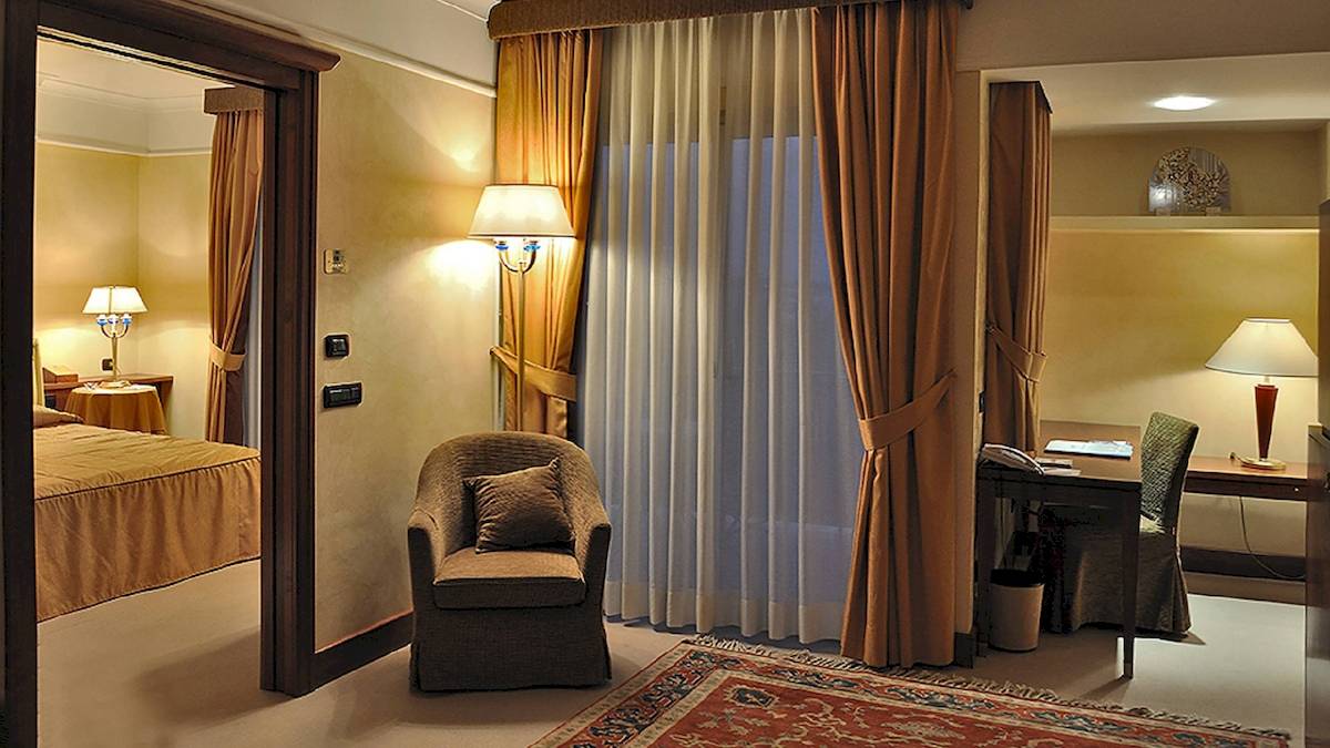 Hotelzimmer im Pineta Palace mit Bett, Stuhl, Schreibtisch und Lampen.