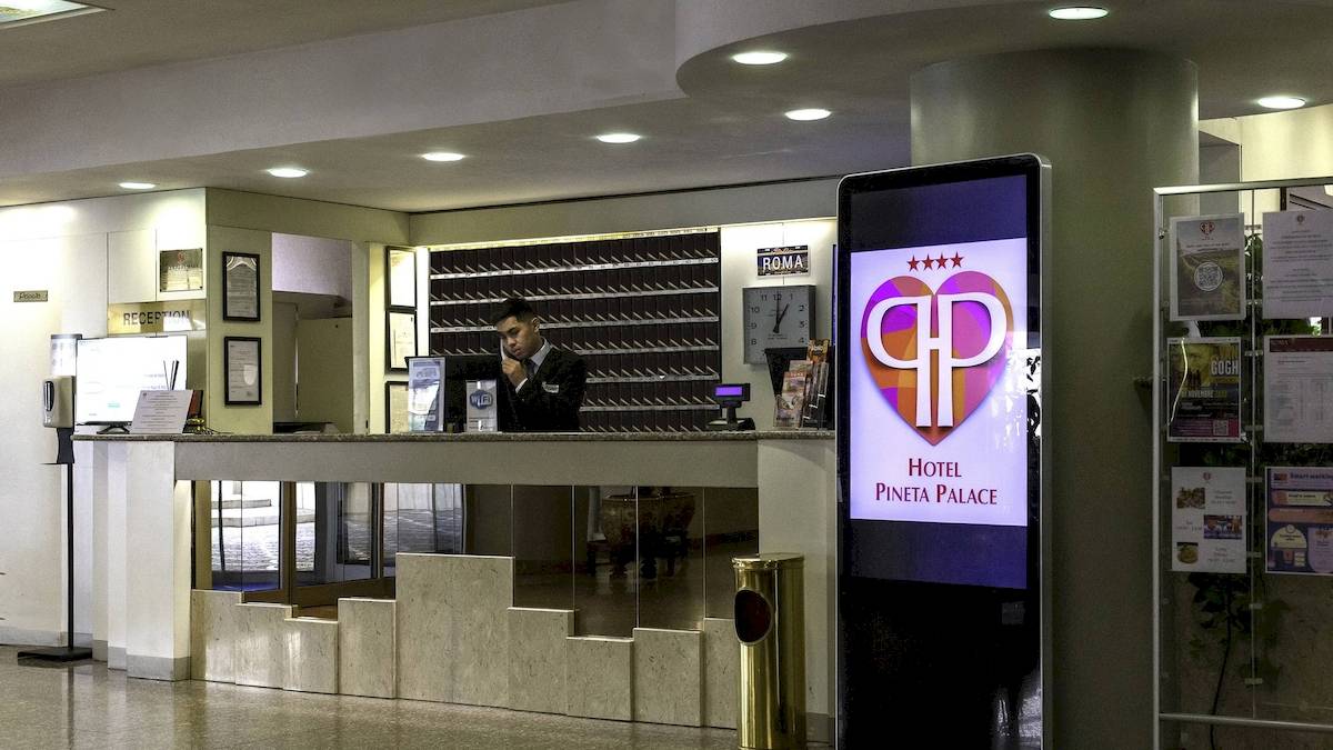 Hotelrezeption mit digitalem Schild und Mitarbeiter, der telefoniert.