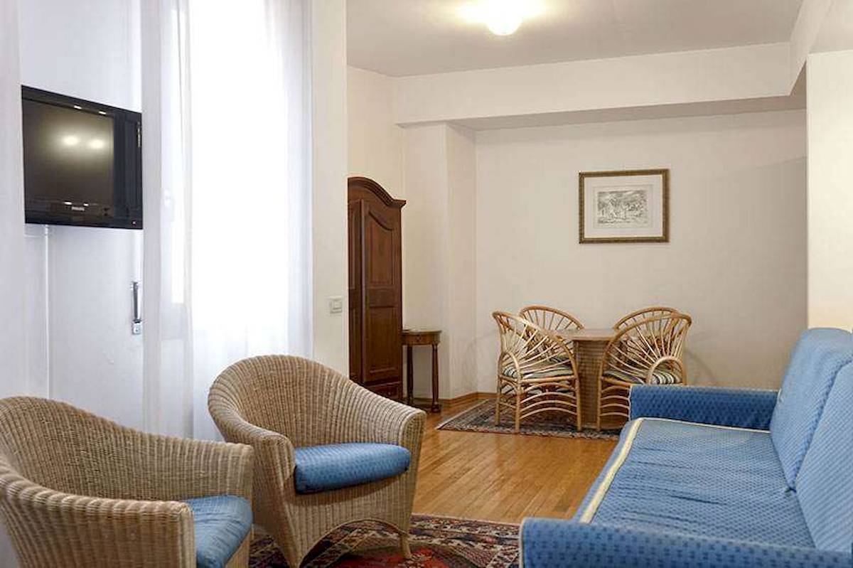 Wohnzimmer im San Marco Palace Hotel mit Fernseher, Korbstühlen und Tisch.