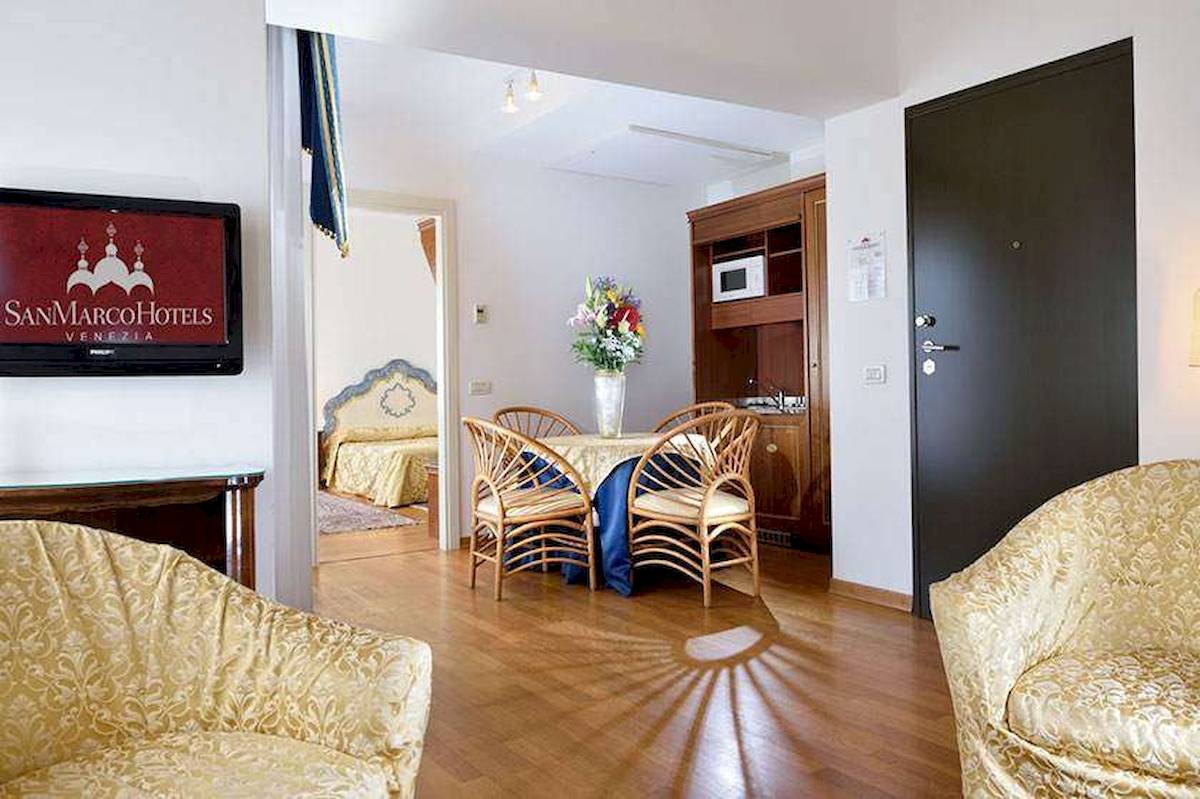 Innenraum des San Marco Palace Hotels mit Wohnzimmer, Esstisch, Fernseher und Schlafzimmer.