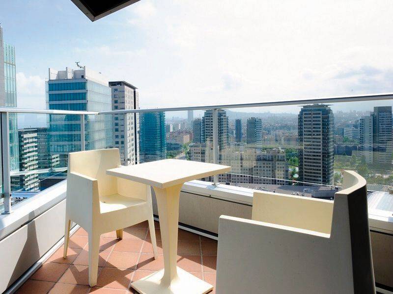 Terrasse mit weißen Stühlen und Tisch, Blick auf die Stadt mit hohen Gebäuden.