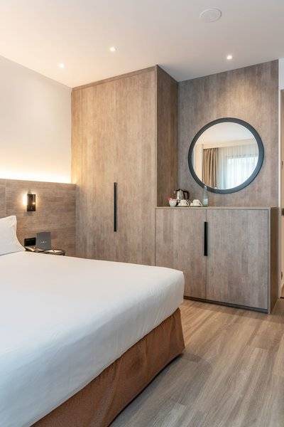Ein modernes Hotelzimmer mit einem Bett, Holzboden und einer Wand mit Spiegel und Einbauschränken.