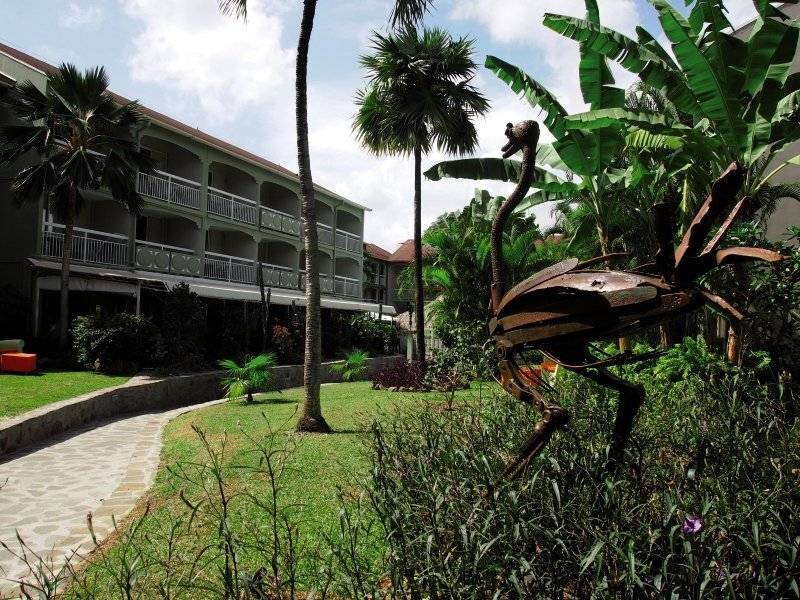 Außenansicht des La Pagerie - Tropical Garden Hotel mit gepflegtem Garten und Flamingoskulptur.