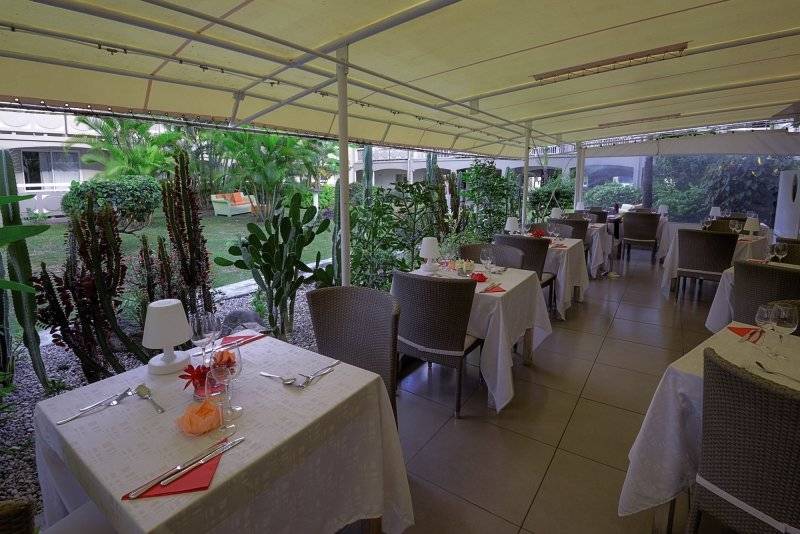 Foto von La Pagerie - Tropical Garden Hotel Restaurant mit Tischen und Stühlen unter einer überdachten Terrasse.