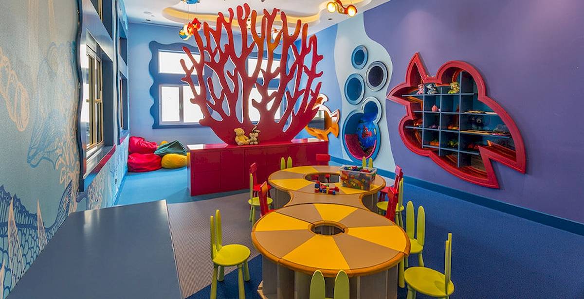 Kinderzimmer im Güral Premier Belek Hotel mit bunten Möbeln, blauen Wänden und einem roten Korallen-Dekor.