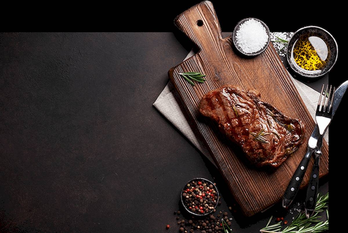 Ein gewürztes Steak liegt auf einem Schneidebrett mit Rosmarin und Gewürzen.