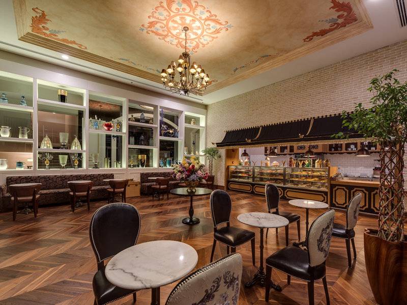 Innenbereich des Rubi Platinum Spa Resort & Suites mit Holzboden, runden Tischen, Stühlen und einer großen Deckenleuchte.