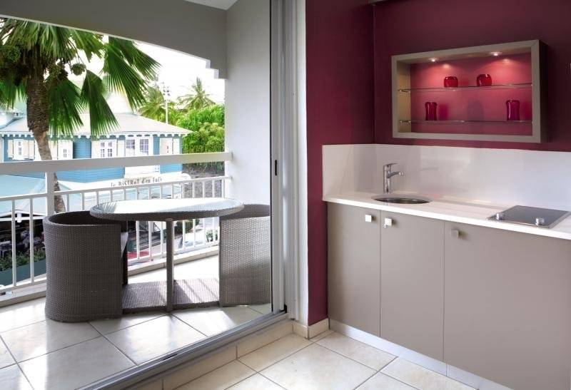 Balkonküche im La Pagerie - Tropical Garden Hotel mit Tisch, Stühlen und Blick auf Palmen und Gebäude.