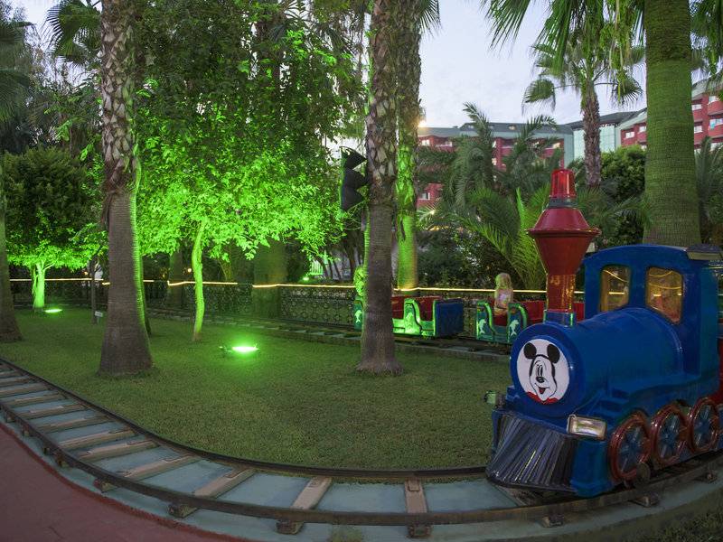 Ein Micky Maus Zug im Delphin Deluxe Hotel Garten mit grünen Lichtern und Bäumen.