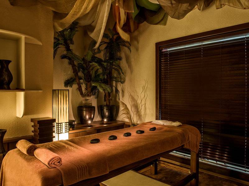 Massageraum im Delphin Deluxe Hotel mit Hocker, Pflanzen und Holzmöbeln.