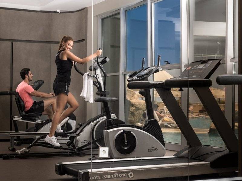 Fitnesscenter im Melas Holiday Village mit Frau auf dem Crosstrainer und Mann auf dem Rudergerät.