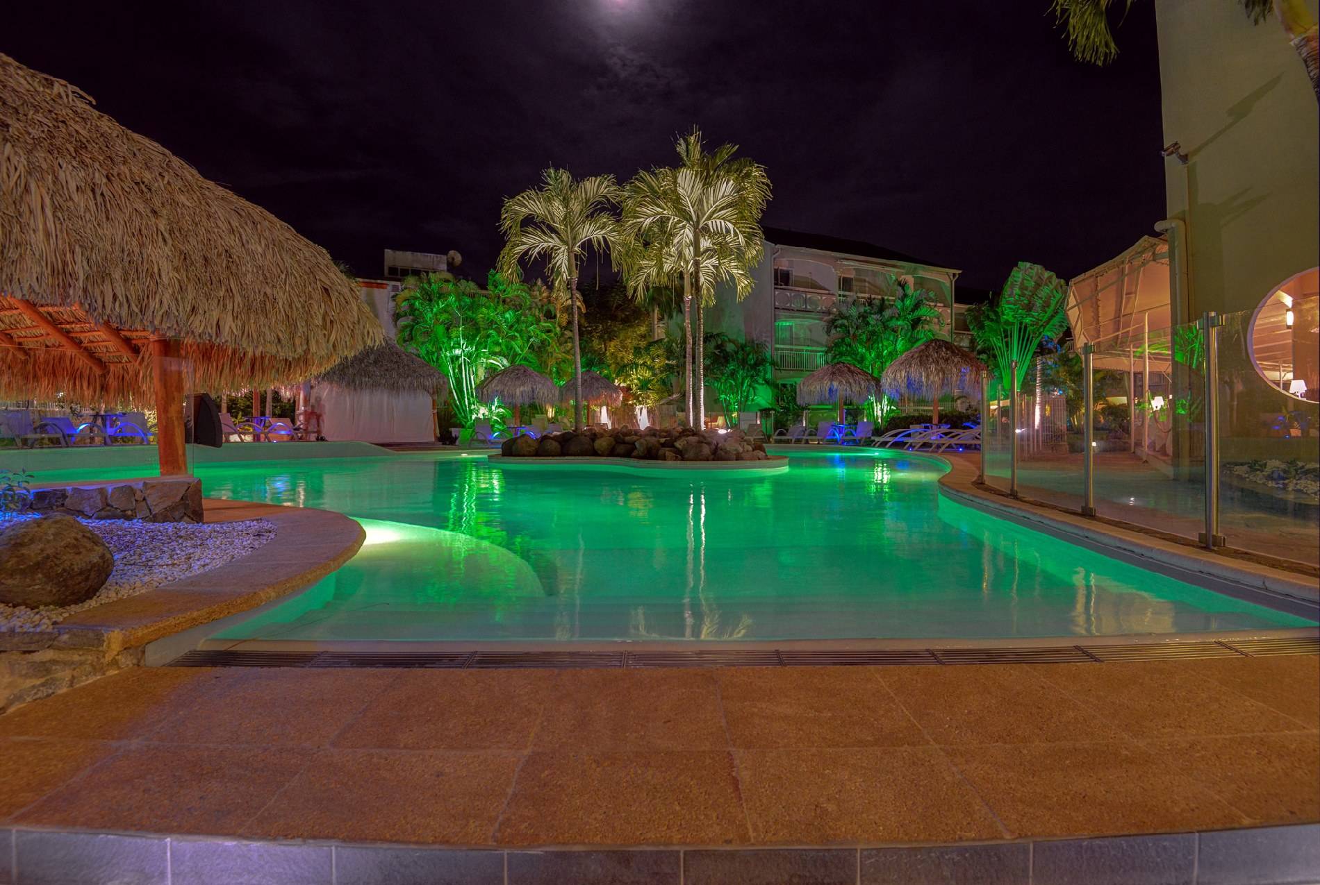 Pool im La Pagerie - Tropical Garden Hotel bei Nacht mit grünen Lichtern und Palmen.
