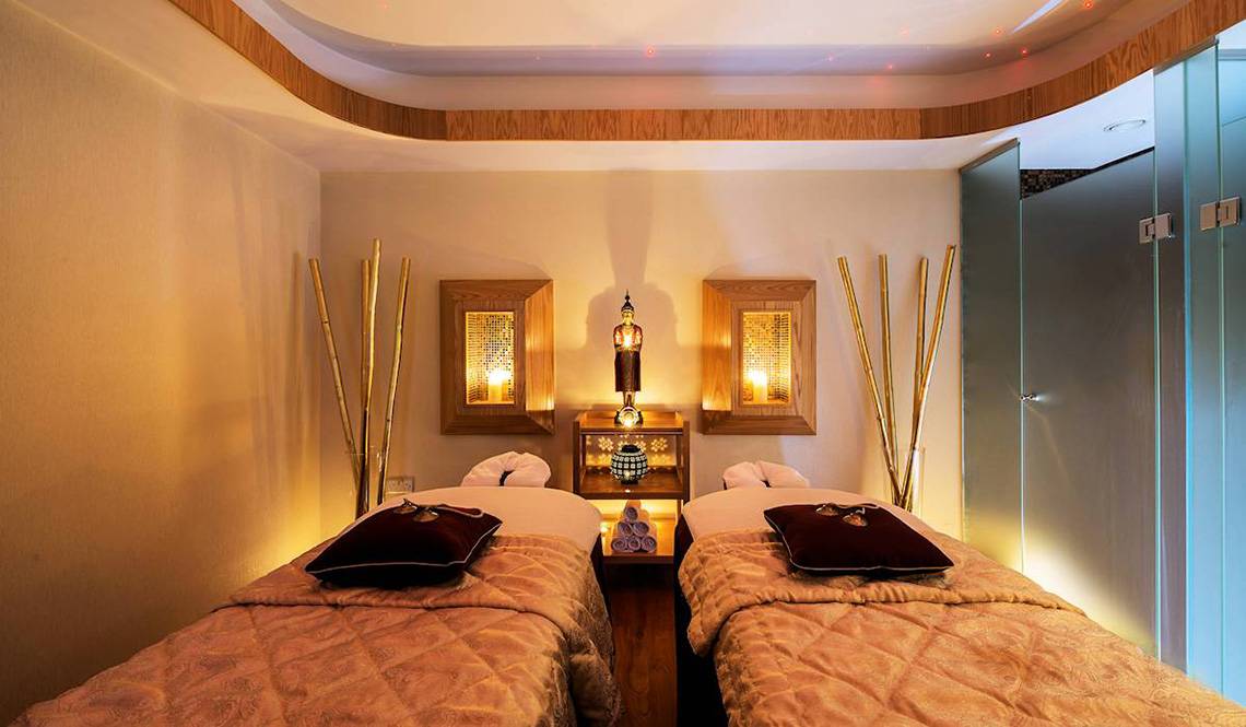 Massagebereich im Constantinou Bros Athena Beach Hotel mit zwei Betten, goldenen Dekorationen und warmem Licht.