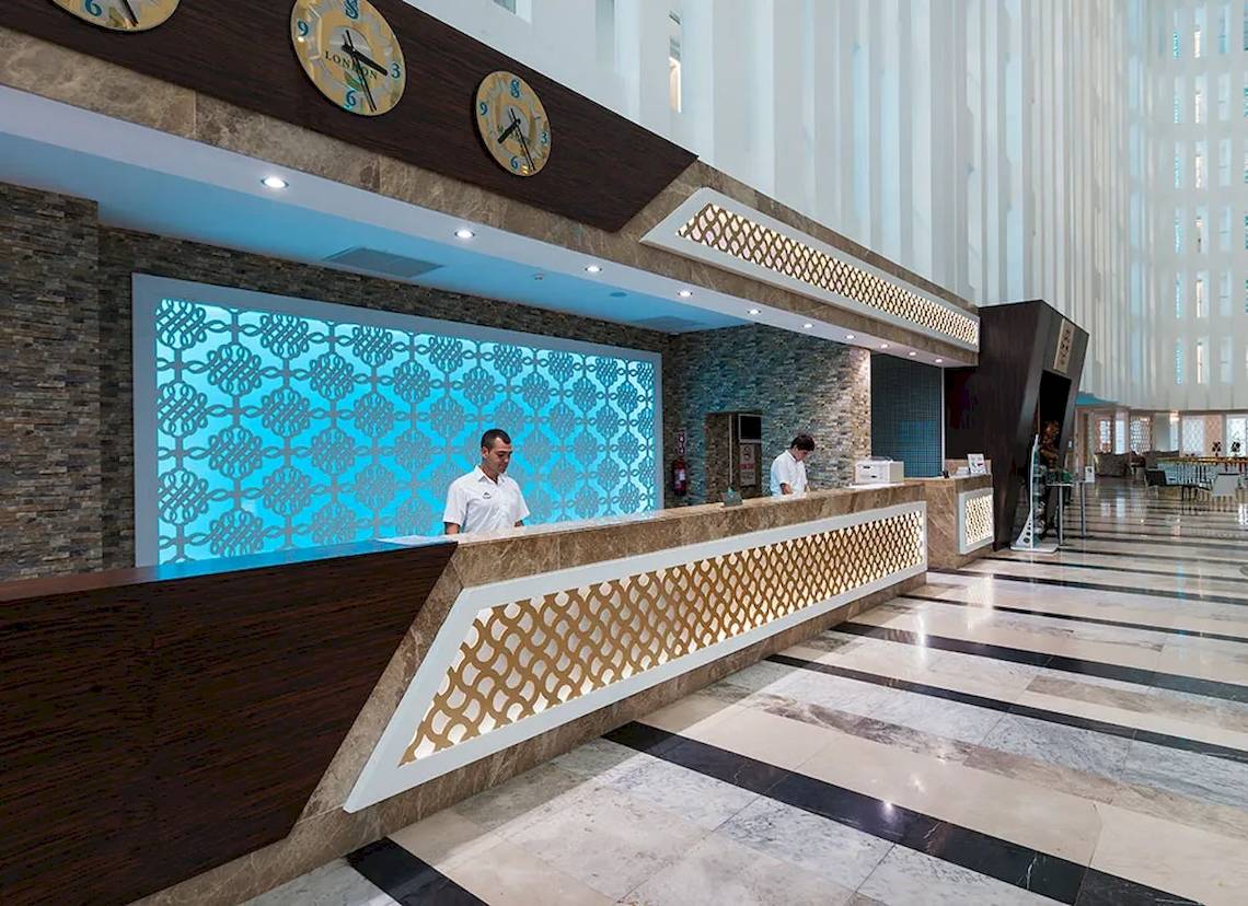 Rezeption des Sultan of Dreams Hotels mit zwei Mitarbeitern an der Rezeption und großen Uhren an der Wand.