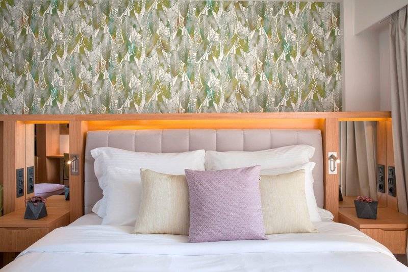 Doppelbett im Hotel Dolce Athens Attica Riviera mit grünen Blatttapeten und weißen Kissen.