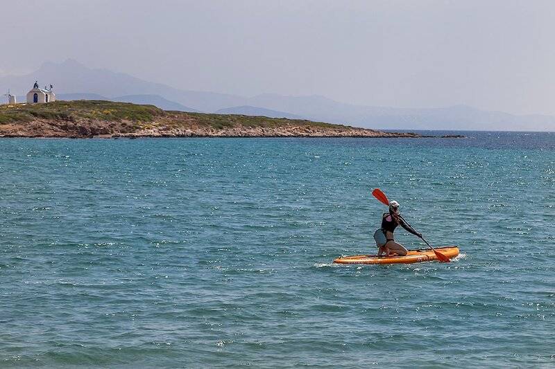 Person paddelt auf einem orangefarbenen SUP-Board im blauen Wasser mit einer kleinen Insel im Hintergrund