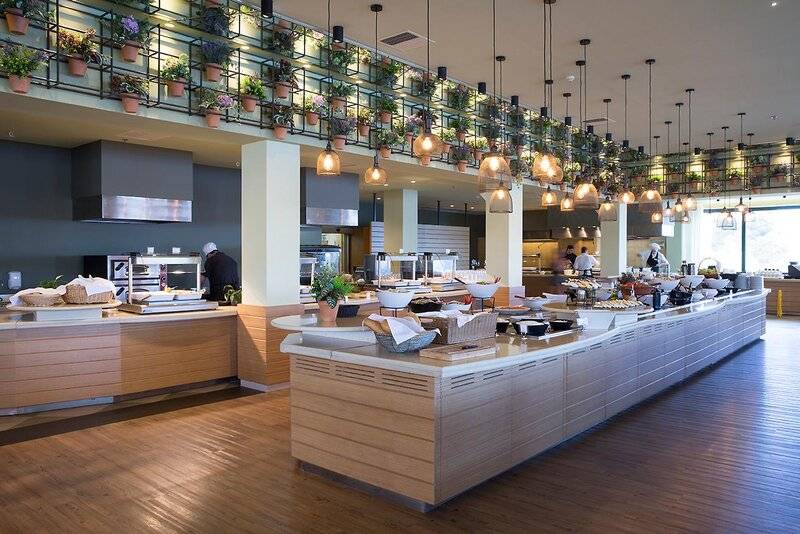 Buffettisch im Hotel Dolce Athens Attica Riviera mit verschiedenen Speisen, Blumenarrangements und Lampen.