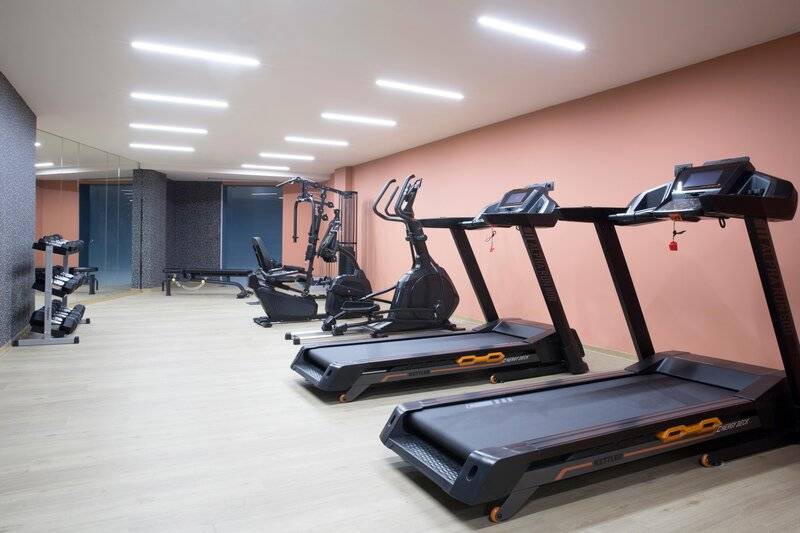Fitnessraum im Hotel Dolce Athens Attica Riviera mit mehreren schwarzen Laufbändern und Trainingsgeräten.
