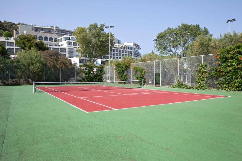 Tennisplatz im Freien am Dolce Athens Attica Riviera Hotel mit rotem Boden und grünem Rand.