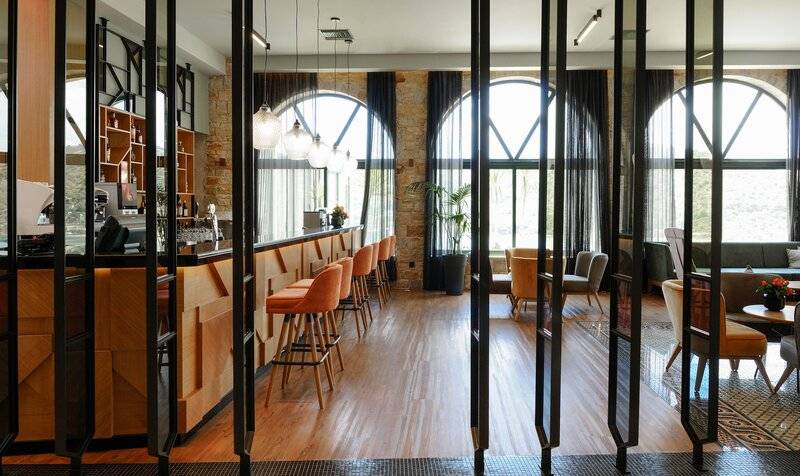 Innenbereich des Dolce Athens Attica Riviera Hotels mit Bar, Stühlen und großen Fenstern.