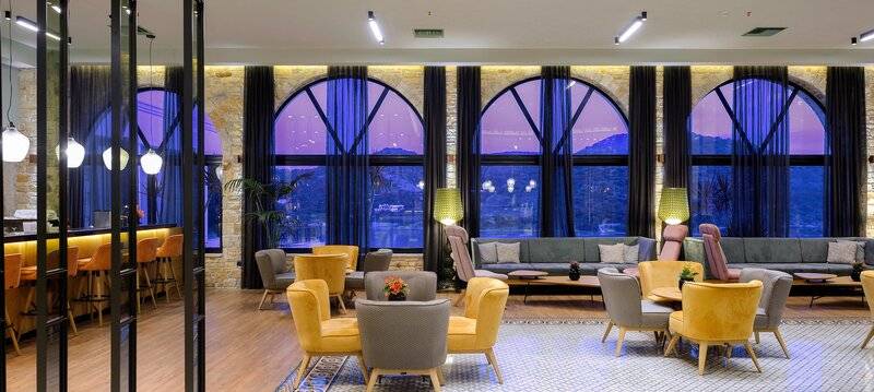 Hotel-Loungebereich des Dolce Athens Attica Riviera mit großen Fenstern und modernen Möbeln.