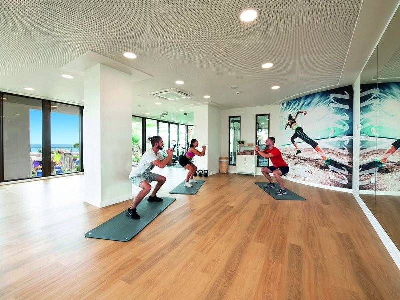 Fitnessraum im Allsun Hotel Sumba mit Personen, die auf Matten trainieren, und einer großen Wandgrafik.