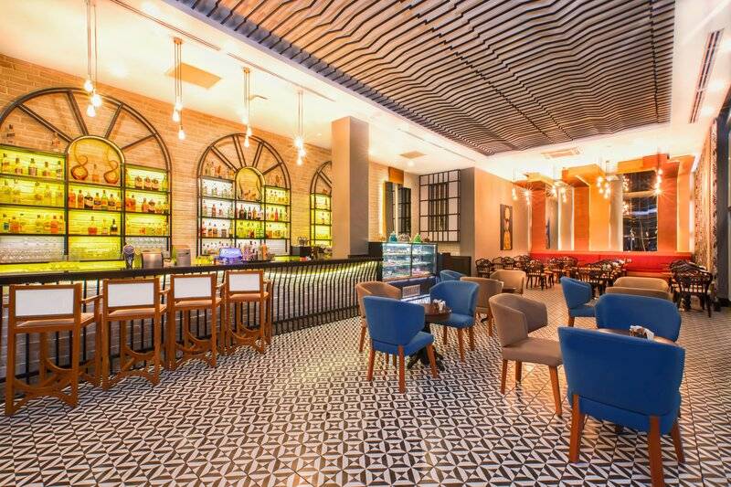 Innenbereich des Sherwood Exclusive Kemer Hotels mit Bar, blauen Stühlen und geometrischem Bodenbelag.